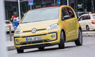 Der VW Up (2016) fährt in einer Stadt um eine Linkskurve, von vorne fotografiert.