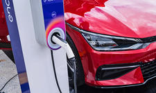 Rotes Elektroauto (Ausschnitt von vorne rechts) auf der rechten Fotoseite, Ladesäule mit angestecktem Kabel auf der linken Fotoseite