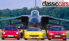 Der Porsche 911 Carrera 2/Ferrari F355/BMW M3 (E36) statisch von vorne vor einem Tornado-Kampfjet fotografiert.