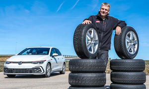 Redakteur Martin Urbanke posiert stolz hinter einem Stapel Reifen, im Hintergrund steht der Testwagen VW Golf GTI.
