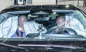Der Innenraum des Audi A5 (2024) ist nach einem Euro NCAP-Crashtest durch die gesprungene Windschutzscheibe fotografiert. Zwei Dummies sitzen inmitten mehrere offener Airbags.