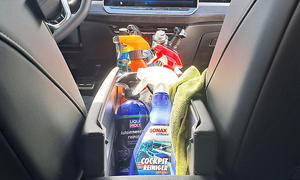 Sprühflaschen mit Cockpitspray und ein Lappen stehen und liegen in der Mittelkonsole eines Testwagens.