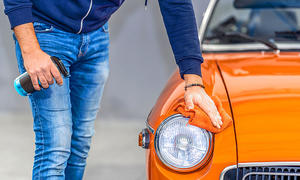 Das Bild zeigt eine Person, die mit einem Auto-Detailer und einem Mikrofasertuch einen Oldtimer reinigt.