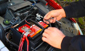 Ein Mann klemmt mithilfe von Werkzeug die 12-V-Batterie im Motorraum eines Autos ab. 