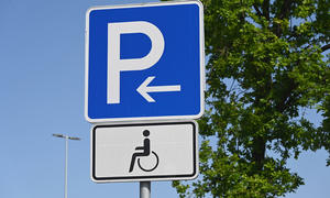 Einen Behindertenparkplatz erkennt man an dem Zusatzschild, das einen Rollstuhlfahrersymbol aufweist. 