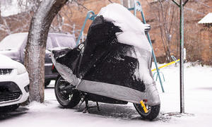 Das Bild zeigt ein geparktes Motorrad unter einer winterfesten Motorradgarage. Um das Motorrad und auf der Plane liegt Schnee.