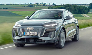 Der Audi Q6 Sportback e-tron (2025) fährt eine Landstraße im Grünen entlang, von vorne links fotografiert.