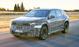 Der BMW iX3 (2026) fährt als Erlkönig eine Straße entlang, von vorne links fotografiert.