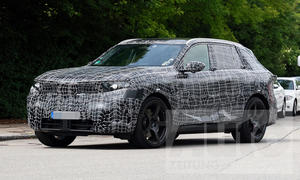 Ein Erlkönig des BMW iX5 M70 xDrive (2026) fährt auf einer Straße, von vorne links fotografiert.