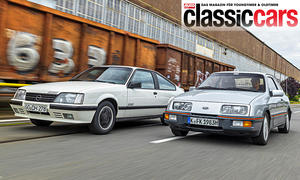 Opel Monza GSE und Ford Sierra XR4i fahren nebeneinander durch ein Industriegebiet, von vorne fotografiert.