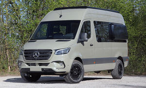 Der Mercedes Sprinter von Vansports steht auf einem Schotterparkplatz, von vorne links fotografiert.