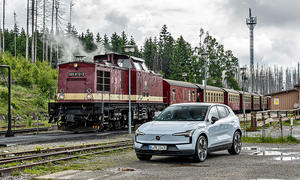 Der Volvo EX30 steht auf einem Schotterplatz, dahinter eine alte Lok mit Wagons.