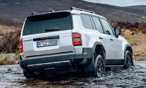 Der Toyota Land Cruiser First Edition (2024) fährt durch Wasser, von schräg hinten fotografiert.