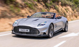 Der Aston Martin Vanquish Volante fahrend von schräg vorne mit offenem Verdeck. Redakteurin Adele Moser am Steuer.