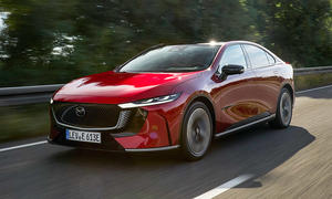 Der Mazda6e (2025) fährt über eine Landstraße, fotografiert von schräg vorne.
