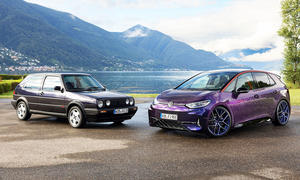 Der VW Golf II Fire+Ice und der VW ID.3 GTX Fire+Ice (2025) stehend, mit der Front zueinander, von vorne fotografiert vor einer See-Berg-Kulisse.