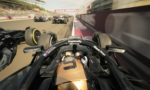 Eine Actionszene zeigt mehrere F1-Autos, die über eine Startgerade fahren. Onboard über dem Kopf des Fahrers aufgenommen.