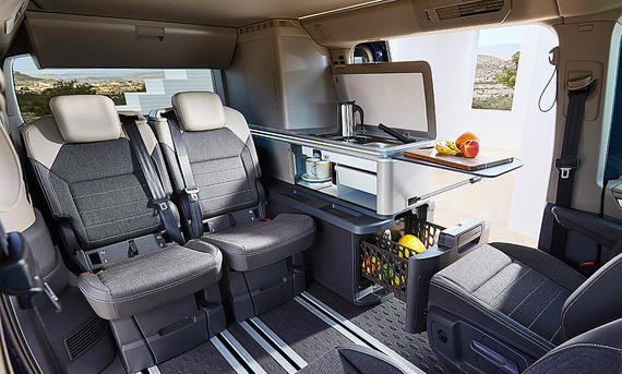 VW California (2024) - VW Das Bild zeigt den Wohnraum des VW California Ocean (2024). Zu sehen ist der Wohnraum mit voller Bestuhlung und Seitenküche mit geöffnetem Kühlschrank.