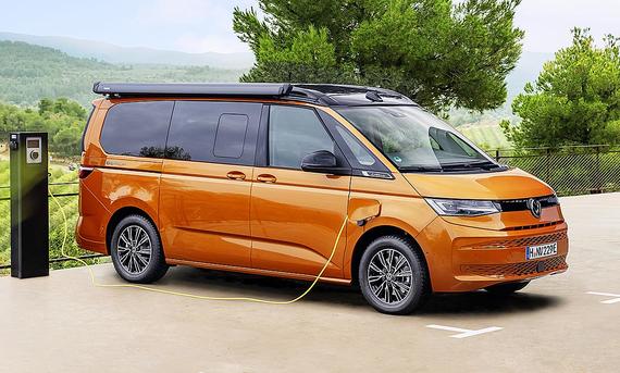 VW California Beach Energy (2025) - VW Das Bild zeigt das Sondermodell VW California Beach Energy (2025) statisch von schräg vorne rechts. Das Fahrzeug mit Plug-in-Hybrid-Antrieb wird an einer Ladesäule geladen.