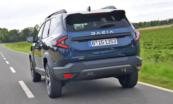 Der Dacia Bigster fährt auf einer Landstraße, von hinten links fotografiert.