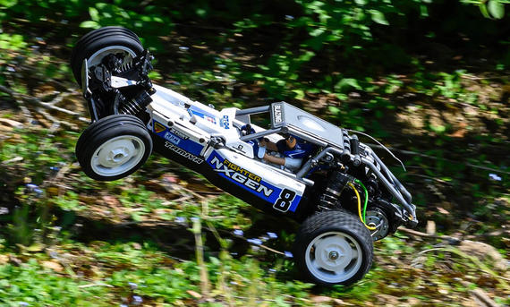Das Bild zeigt das RC-Auto Tamiya DT-04 Fighter Nxgen fahrend von schräg vorne links fotografiert. Die Vorderräder sind in der Luft, da das Fahrzeug über eine kleine Graskuppe springt.