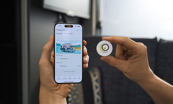 Eriba Novaline (2025) - Eriba Das Bild zeigt die Smartphone-Steuerung per Eriba-App im Eriba Novaline (2025). Im Foto hält eine Person ein Smartphone sowie einen Button mit der Aufschrift "E-Trailer".