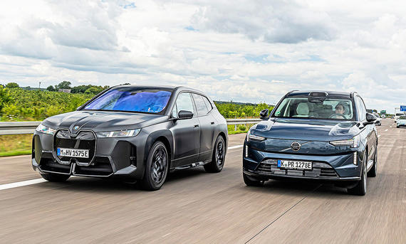 Blick von vorne auf die beiden Elektroautos BMW iX und Volvo EX90, die auf der Autobahn nebeneinander her fahren.