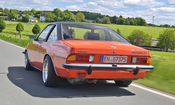 Der Opel Manta B 1.9 E fährt über eine Landstraße, von schräg hinten fotografiert.