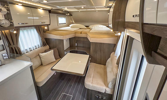 Phoenix Midi Alkoven 6700 HBL (2025) - Phoenix Reisemobile Das Bild zeigt den Wohnraum des Phoenix Midi Alkoven 6700 HBL (2025). Zu sehen ist die Sitzgruppe und das Alkovenbett. Der Zugang zum Fahrerhaus ist geschlossen.