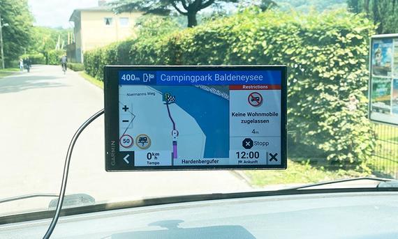 Das Innenaufnahme zeigt das Garmin-Navi im Testeinsatz an der Windschutzscheibe einem VW-Busses. Auf dem Display wird der Zielort, ein Campingplatz, in Essen gezeigt.