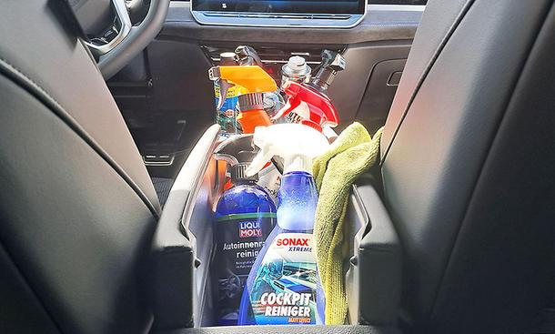 Sprühflaschen mit Cockpitspray und ein Lappen stehen und liegen in der Mittelkonsole eines Testwagens.