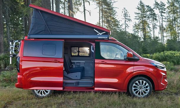 Die Außenaufnahme zeigt den Ford Transit Custom Nugget (2024) von der Seite auf einer Wiese mit aufgestelltem Dach.