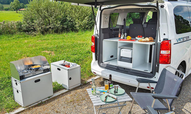 Das Bild zeigt die Campingbox "Kitchen" des Pössl Vanster im Detail. Vor der geöffneten Heckklappe stehen Campingmöbel.