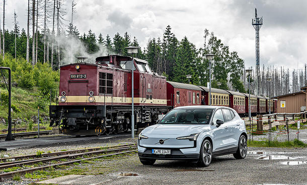 Der Volvo EX30 steht auf einem Schotterplatz, dahinter eine alte Lok mit Wagons.