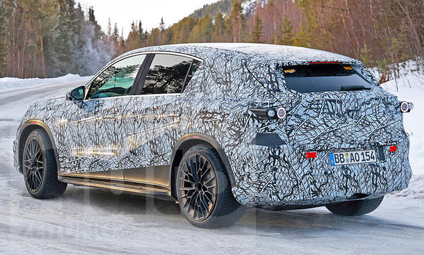 Der Mercedes-AMG GLC EQ (2026) fährt als Erlkönig über eine verschneite Straßen, von hinten links fotografiert.