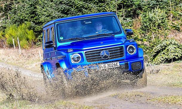 Blick von schräg vorne auf den fahrenden Mercedes G 580 EQ, der gerade durch eine tiefe Matschpfütze fährt.