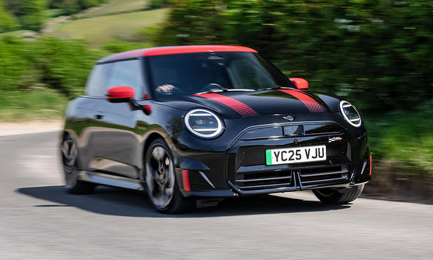 Der Mini JCW Electric (2025) fährt dynamisch durch eine Kurve, fotografiert von schräg vorne.