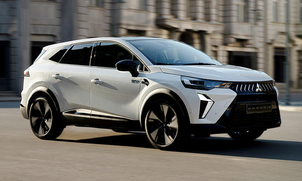 Der Mitsubishi Grandis (2025) fahrend von schräg vorne fotografiert vor einer städtischen Kulisse.