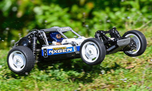 Das Bild zeigt das RC-Auto Tamiya DT-04 Fighter Nxgen fahrend von schräg vorne rechts fotografiert. Die Vorderräder sind in der Luft, da das Fahrzeug über eine kleine Graskuppe springt.