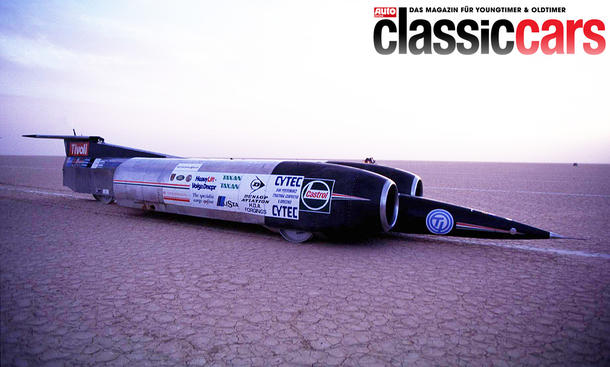 Das Hochgeschwindigkeitsauto ThrustSSC steht in einer Wüste, von vorne rechts fotografiert.