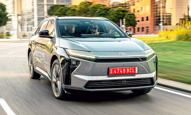 Das Toyota bZ4X Facelift (2025) fährt in einer Stadt durch einen Kreisverkehr, von vorne fotografiert.