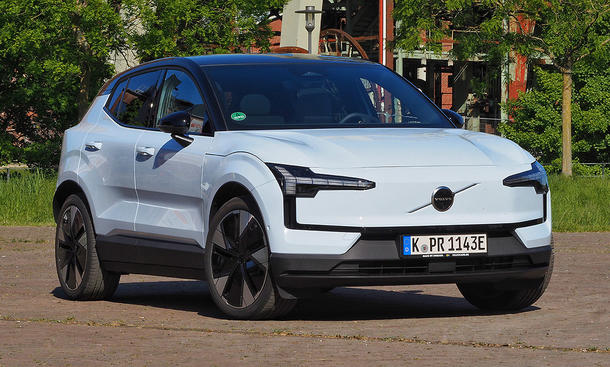 Der Volvo EX30 Single Motor Extended Range Ultra steht vor einem Gebäude im Grünen, Ansicht von vorne rechts.