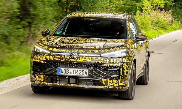 Der VW T-Roc (2025) fährt mit Tarnfolie auf einer Landstraße, von vorne fotografiert.