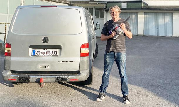 Die Außenaufnahme zeigt einen Tester mit dem Dyson Akku-Staubsauger Car & Boat V8 in der Hand vor einem silbernen VW Bus.