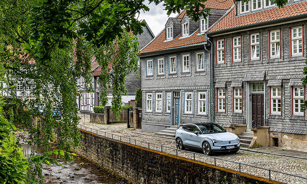 Der Volvo EX30 steht vor einem alten Gebäude in Goslar, davor fließt wenige Meter tiefer ein kleiner Fluss.