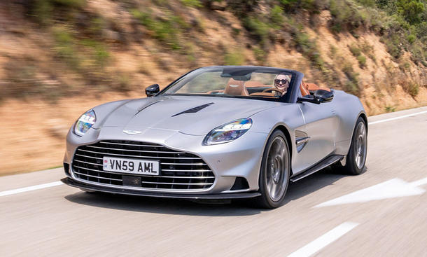 Der Aston Martin Vanquish Volante fahrend von schräg vorne mit offenem Verdeck. Redakteurin Adele Moser am Steuer.
