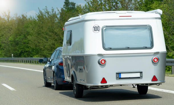 Ein Auto fährt über eine Straße und zieht einen kleinen Caravan.