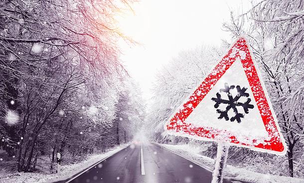 Eine verschneite Straße mit einem Verkehrszeichen rechts unten.