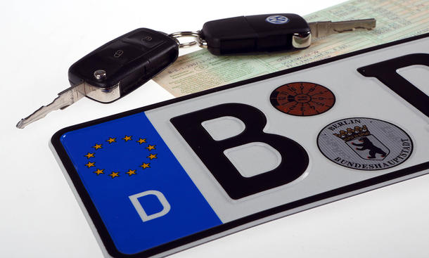 Auto online anmelden/zulassen: Symbolbild zeigt zwei Autoschlüssel auf Fahrzeugpapieren und einem Kennzeichen.