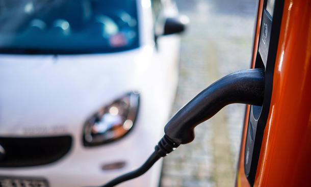 Ein Ladekabel eines E-Autos und im Hintergrund sieht man einen Smart, parkend.